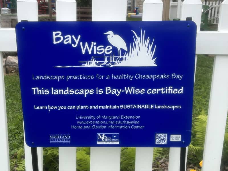 Sign promoting Bay-Wise certified sustainable landscaping by University of Maryland Extension, featuring garden practices for Chesapeake Bay health, with a blue background.
