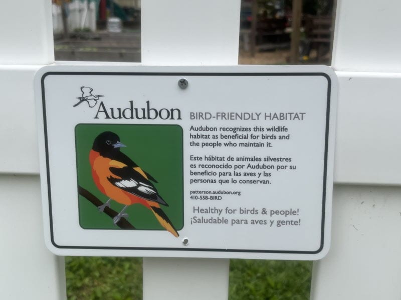 Sign on a fence from Audubon, recognizing a bird-friendly habitat, beneficial for birds and people. Features a vibrant bird illustration.