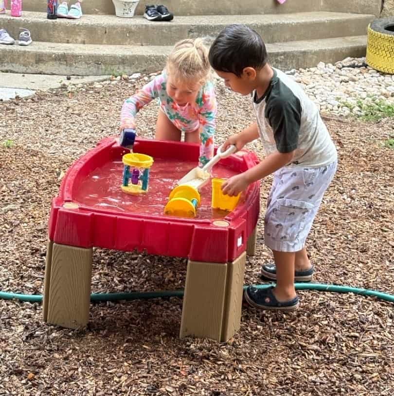 Children playing with water table at Trinity Episcopal Preschool, engaging in outdoor sensory and social activities.