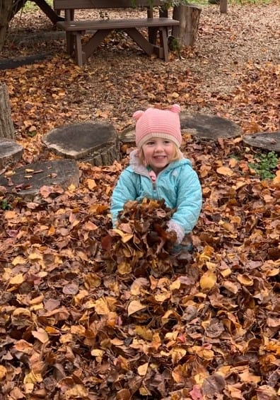 Happy young girl playing in autumn leaves at Trinity Episcopal Preschool, outdoor fall scene, children’s outdoor activities, preschool playground, seasonal outdoor play.