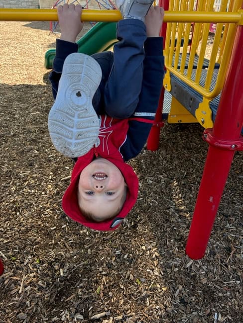 Child hanging upside down on playground equipment.