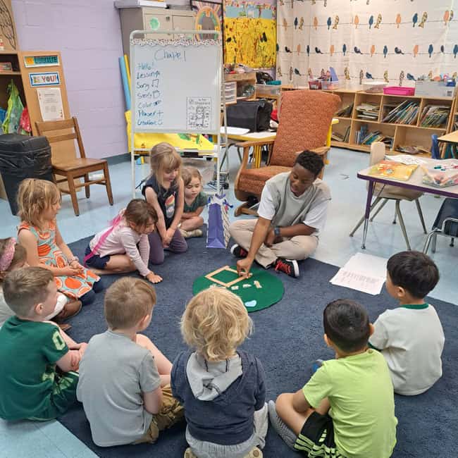 Young children sitting on the carpet in a preschool classroom, engaging with a teacher during a learning activity at Trinity Episcopal Preschool.